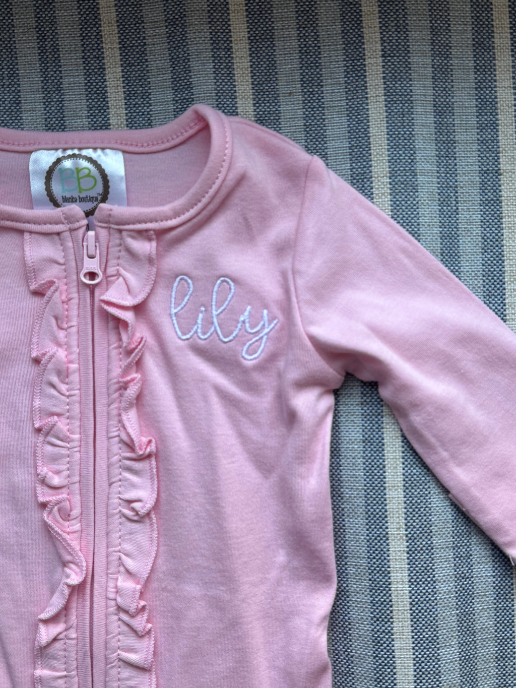 Pink baby outfit with 'lily' monogram on a striped background